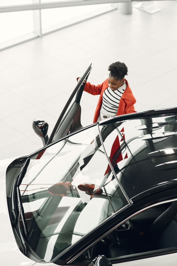 High angle view of woman inspecting sleek black car indoors. Stylish auto showroom.